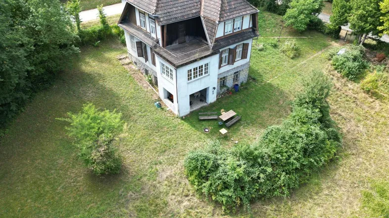 Luftaufnahme eines älteren Hauses mit großem Garten und umliegender grüner Landschaft.