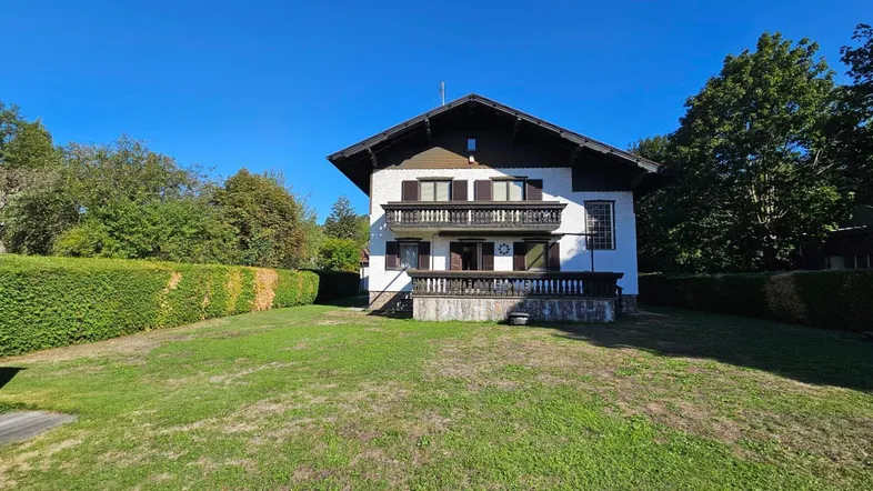 Traditionelles Haus mit weißer Fassade, Holzbalkonen und großem, gepflegtem Gartenbereich.