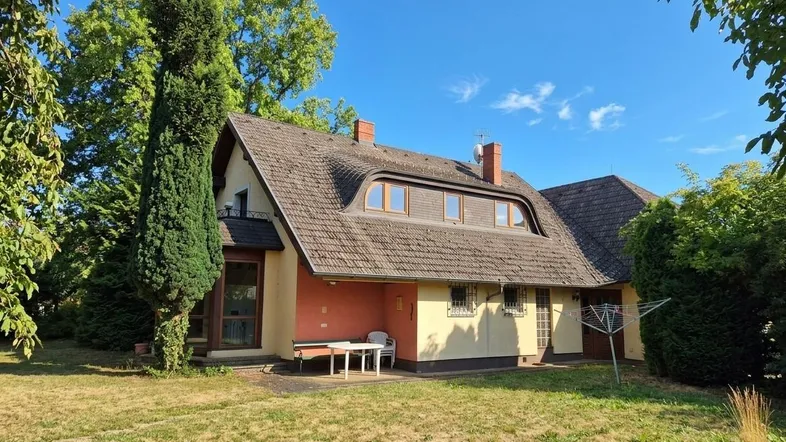 Großzügiger Gartenbereich hinter dem Haus mit Rasenfläche und kleiner Terrasse unter Bäumen.