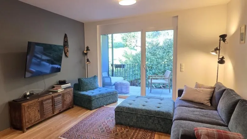 Helles Wohnzimmer mit Holzboden, gemütlicher Sitzecke und Zugang zu einem Balkon.