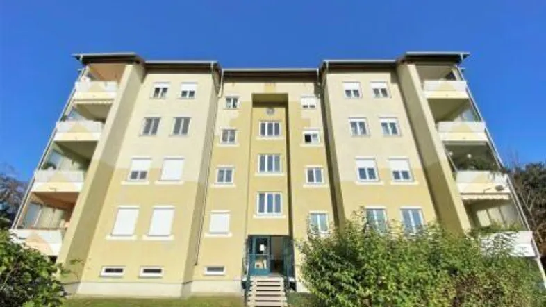 Mehrfamilienhaus mit mehreren Balkonen und gepflegter Grünfläche vor dem Eingangsbereich.
