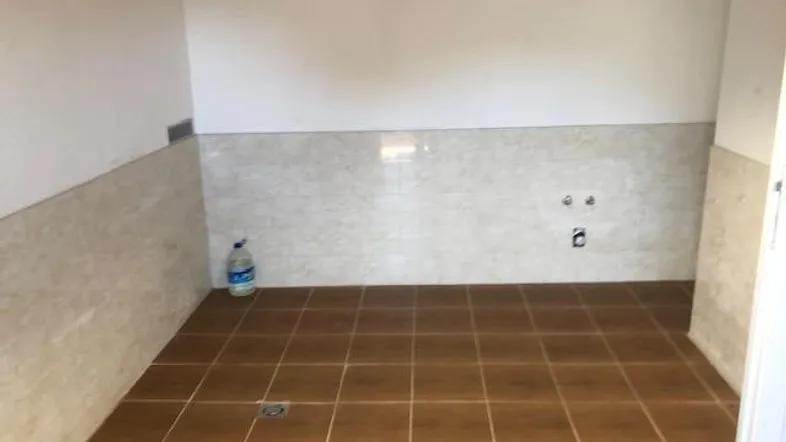 Leerer Raum mit braunen Bodenfliesen und halbhohen Wandfliesen, vorbereitet für Wasseranschlüsse.