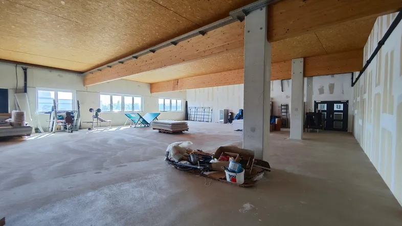 Großer, heller Gewerberaum im Rohbau mit Holzbalkendecke und vielen Fenstern, bereit für den Ausbau.