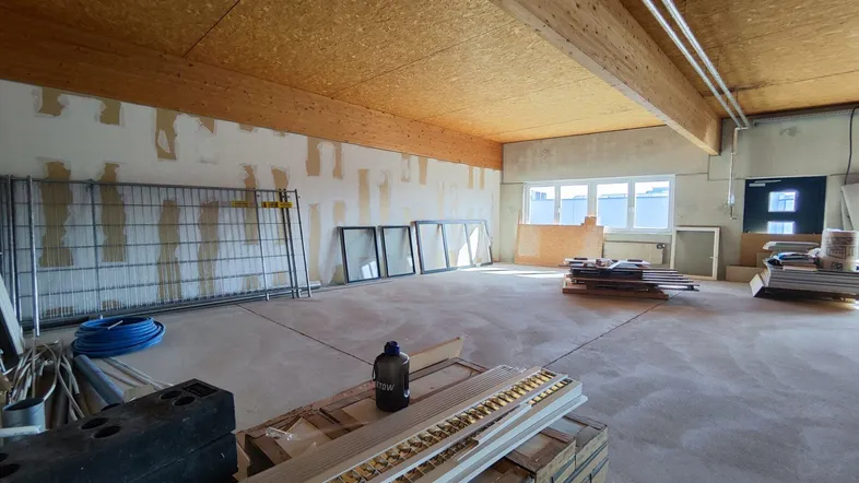 Großer, unfertiger Innenraum mit Holzbalkendecke und Betonboden, bereit für den Ausbau.