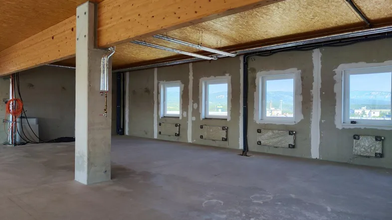 Unfertiger Innenraum mit sichtbaren Holzträgern, Betonpfeiler und Fenstern, die eine weite Aussicht bieten.