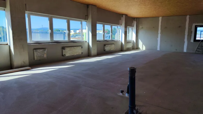 Großer, heller Raum im Rohbauzustand mit vielen Fenstern und Betonboden, bereit für den Ausbau.