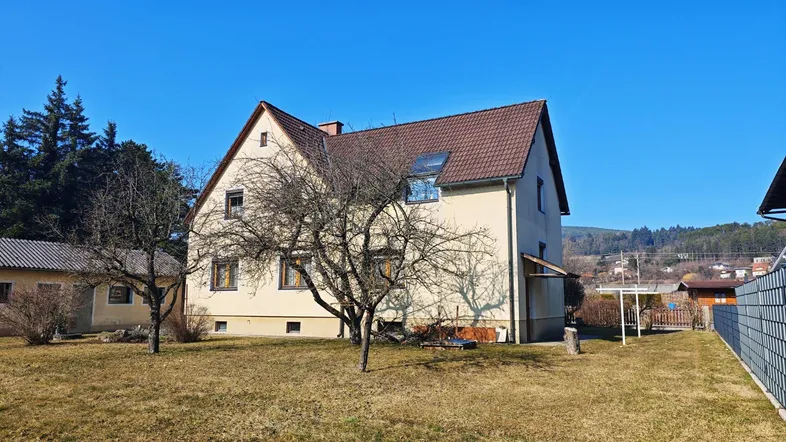 Einfamilienhaus mit Satteldach und großem Gartenbereich unter blauem Himmel.