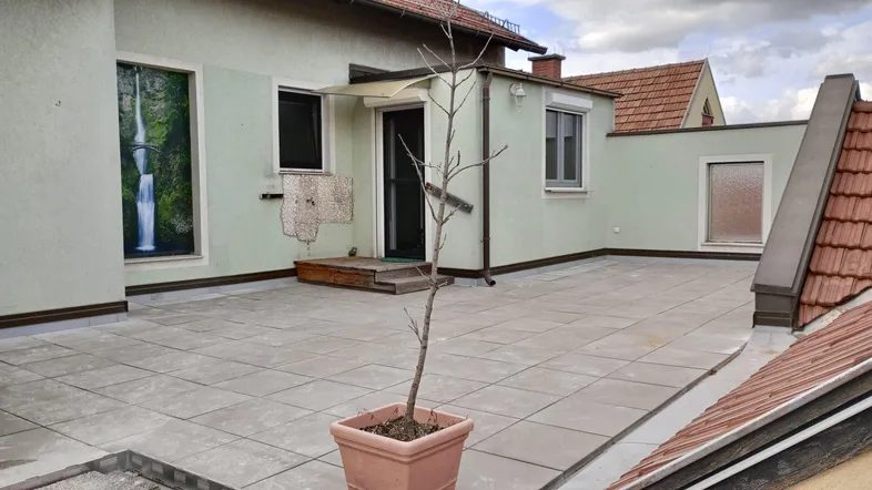 Große, geflieste Dachterrasse mit Zugang zum Gebäude und Blick auf die umliegenden Dächer.