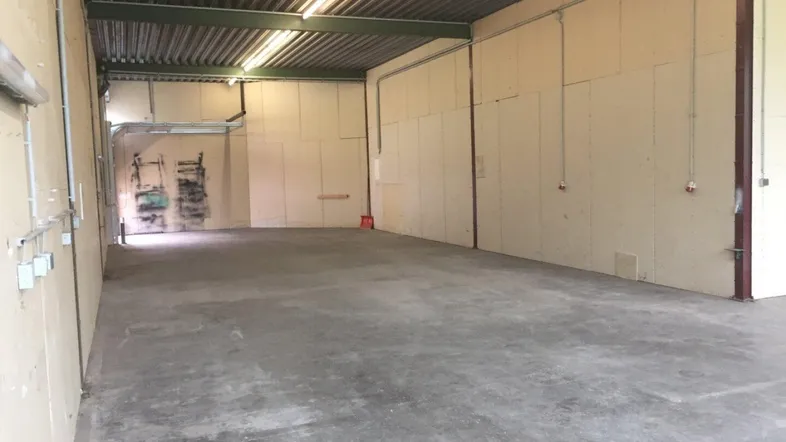 Geräumige, leere Lagerhalle mit Betonboden, hohen Decken und Wellblechdach.