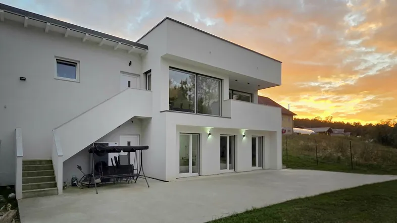 Moderne weiße Villa mit großen Fenstern und einer weitläufigen Terrasse bei Sonnenuntergang.