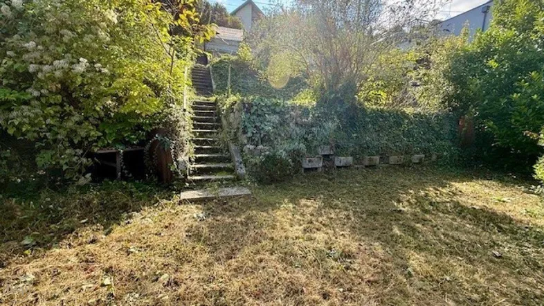 Ungepflegter Gartenbereich mit alten Steinstufen und üppiger Vegetation, die auf eine Renovierung wartet.