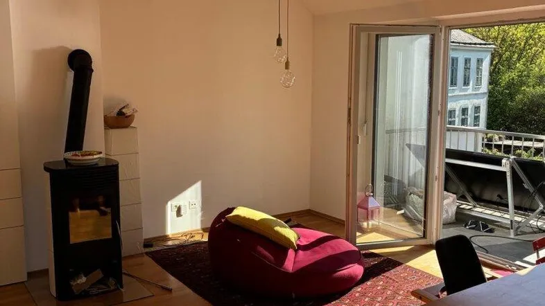 Helles Wohn- und Esszimmer mit Holzboden, Kaminofen und Zugang zum sonnigen Balkon.