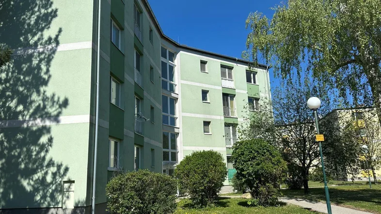 Grünes Mehrfamilienhaus mit mehreren Stockwerken und Balkonen in sonniger Umgebung.