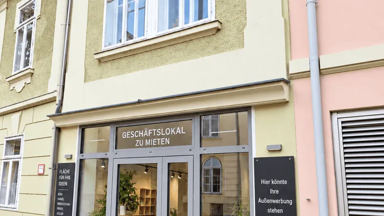 Fassade eines historischen Gebäudes mit einem Geschäftslokal im Erdgeschoss und großen Fenstern im Obergeschoss.