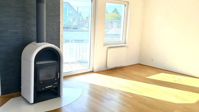 Helles Wohnzimmer mit modernem Kaminofen, Holzboden und Zugang zum Balkon.