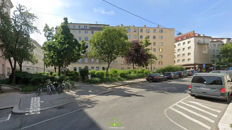 Blick auf die Straße mit parkenden Autos und umliegenden Wohngebäuden.