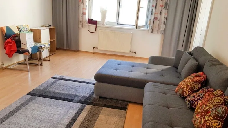 Helles Wohnzimmer mit großem Ecksofa, Teppich und Fenster mit Vorhängen.