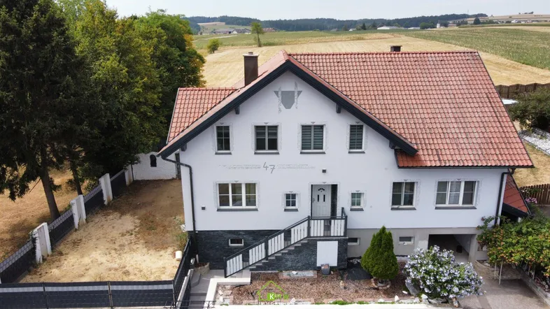 Freistehendes Einfamilienhaus mit rotem Ziegeldach und ländlicher Umgebung, umgeben von Bäumen.