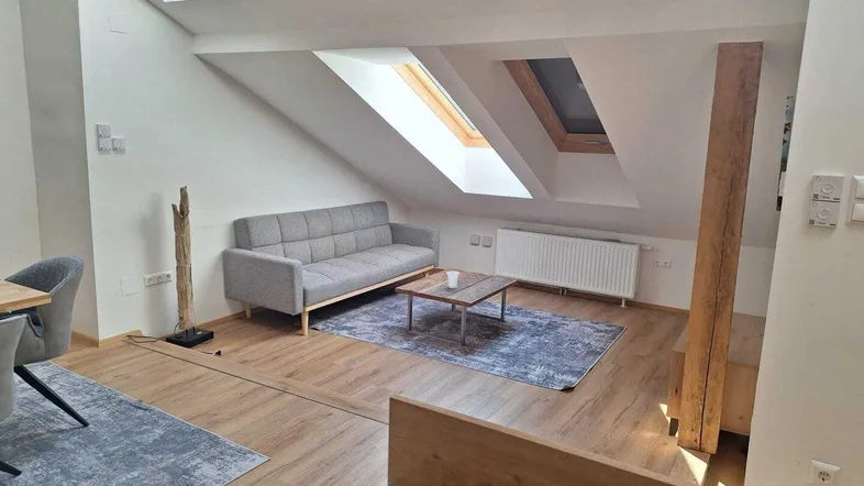 Helles Dachgeschoss-Wohnzimmer mit gemütlichem Sofa, Holzbalken und Dachfenstern für viel Tageslicht.