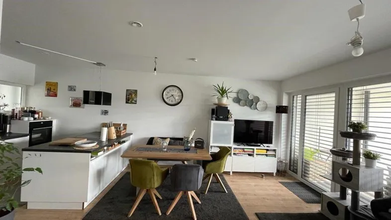 Heller offener Wohn-Essbereich mit integrierter Küche, Holzboden und Zugang zum Balkon.