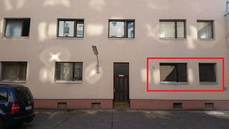 Fassade eines Mehrfamilienhauses mit mehreren Fenstern und Eingangstür im Erdgeschoss.