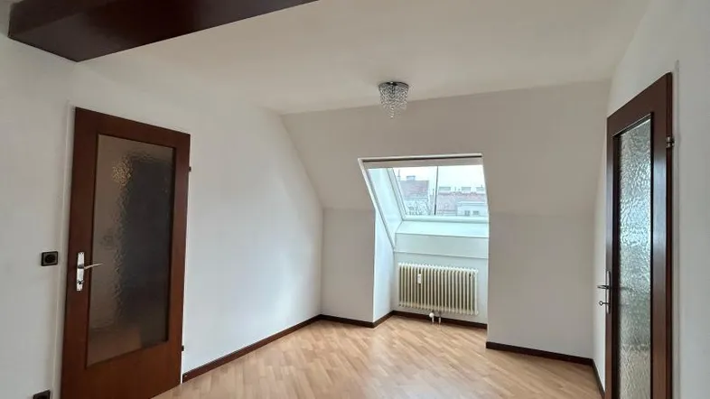 Heller Raum im Dachgeschoss mit Holzbalken, Laminatboden und Dachfenster, der viel Potenzial bietet.
