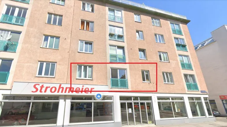Außenansicht eines Mehrfamilienhauses mit Geschäften im Erdgeschoss und einem hervorgehobenen Bereich.