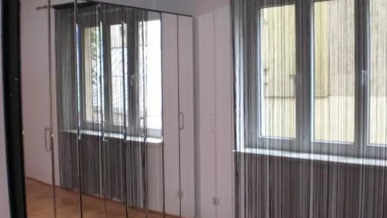 Schlafzimmer mit großem Spiegelschrank, Holzfußboden und Fenstern mit Vorhängen.