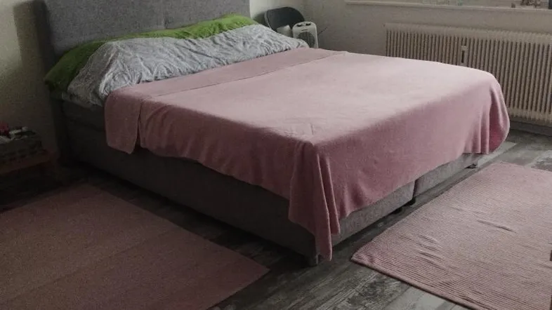 Gemütliches Schlafzimmer mit großem Bett, Laminatboden und Fenster mit Jalousien.