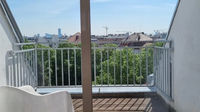 Heller Balkon mit Holzboden und weitem Blick über die Stadt und grüne Bäume.