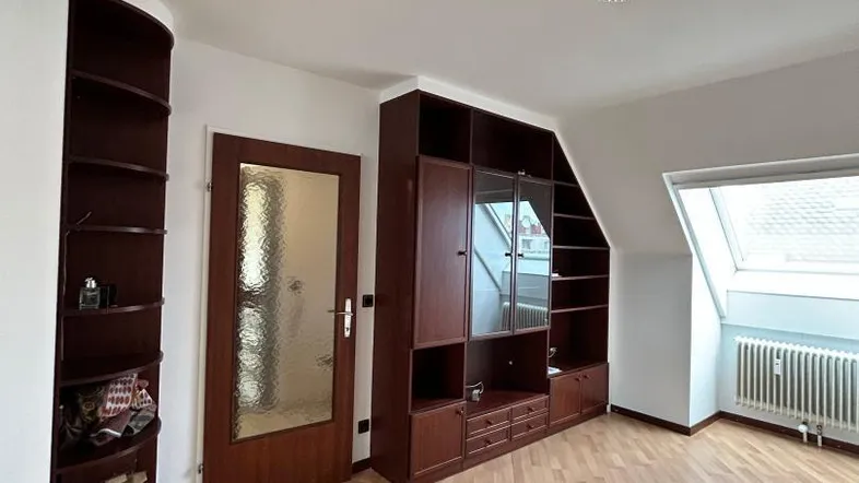Helles Zimmer im Dachgeschoss mit Einbauregalen, Laminatboden und Dachfenster.