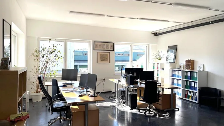 Helles und geräumiges Büro mit mehreren Arbeitsplätzen, großen Fenstern und modernem Betonboden.