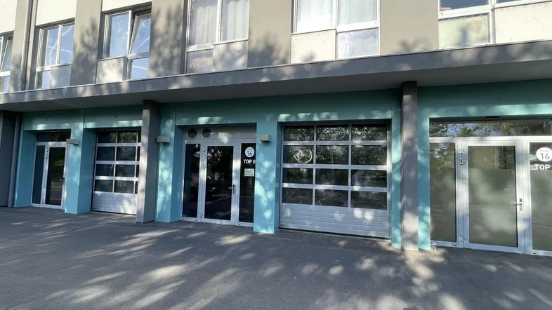 Ansicht der Gebäudefassade mit mehreren Eingängen und Garagentoren im Erdgeschossbereich des modernen Gebäudes.