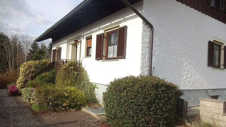 Traditionelles Einfamilienhaus mit weißer Fassade, braunen Fensterläden und gepflastertem Weg im Vorgarten.