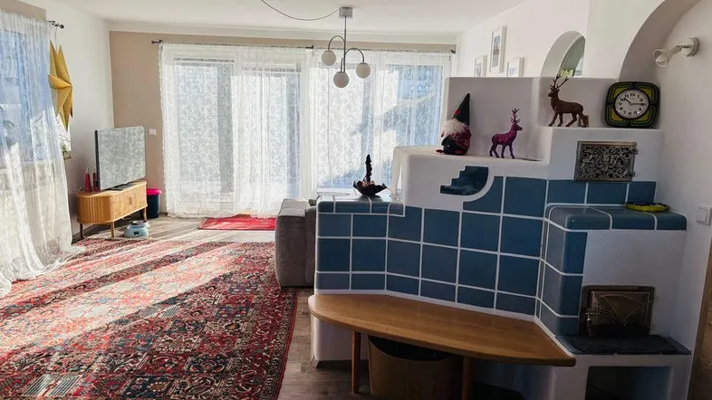 Helles Wohnzimmer mit gemütlichem Kachelofen, integrierter Sitzbank und großem Teppich.