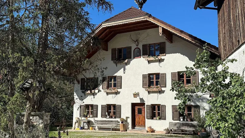 Traditionelles Bauernhaus mit Holzbalkonen und Fensterläden unter blauem Himmel.