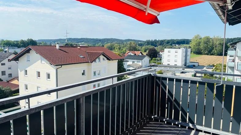 Geräumiger Balkon mit roter Markise und weitem Blick über die umliegende Wohngegend.