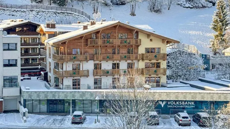 Mehrstöckiges Gebäude im alpinen Stil mit Holzbalkonen und schneebedeckter Umgebung.