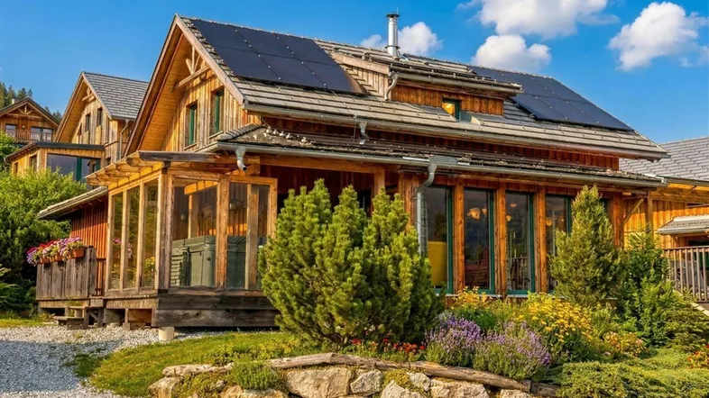 Charmantes Holzhaus mit Solarpaneelen auf dem Dach und gepflegtem Vorgarten unter blauem Himmel.