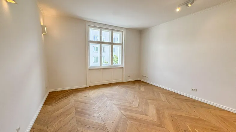 Helles Zimmer mit elegantem Fischgrätparkett, hohen Decken und weiß gestrichenen Wänden.