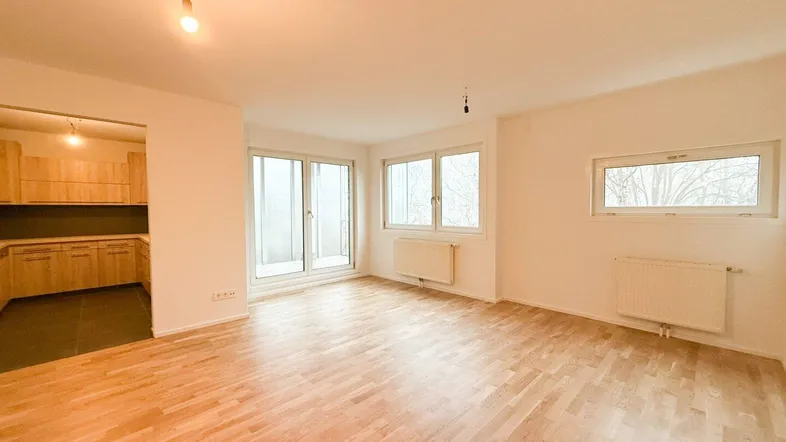 Helles Wohnzimmer mit offenem Küchenbereich, Parkettboden und Zugang zum Balkon.