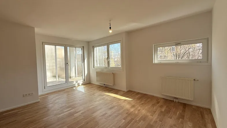 Geräumiger Wohnraum mit Parkettboden, großen Fenstern und direktem Zugang zum Balkon.
