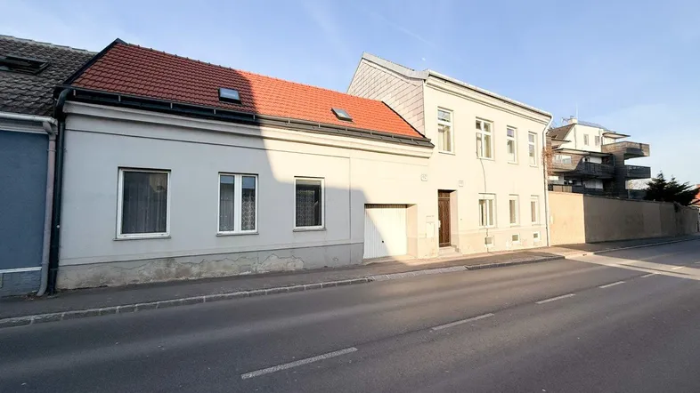 Fassade eines Wohnhauses mit rotem Ziegeldach und Garageneinfahrt von der Straße aus.