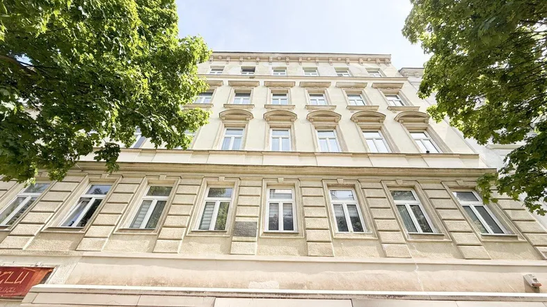 Historisches Mehrfamilienhaus mit klassischer Fassade und vielen Fenstern unter blauem Himmel.