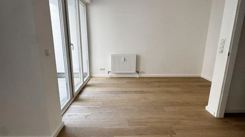 Helles Zimmer mit Holzboden und Zugang zu einem Balkon, ideal als Wohn- oder Schlafbereich.