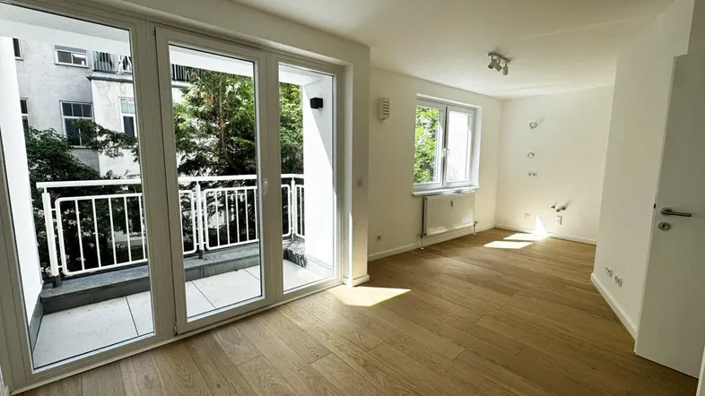 Helles Zimmer mit Holzboden, großen Fenstern und Zugang zu einem Balkon mit Blick ins Grüne.