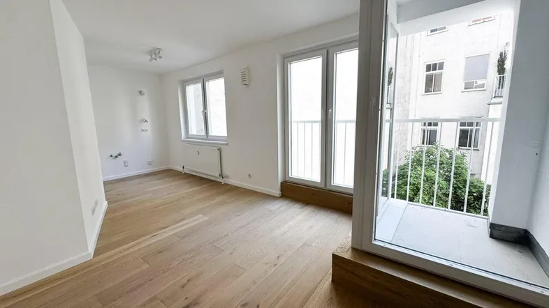 Helles Zimmer mit Holzboden, weißen Wänden und Zugang zu einem kleinen Balkon.