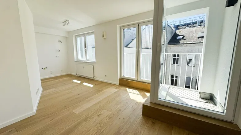 Helles Zimmer mit Holzboden und Zugang zu einem kleinen Balkon, ideal als Wohn- oder Schlafbereich.
