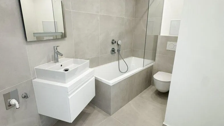 Modernes Badezimmer mit hellgrauen Fliesen, Badewanne mit Duschbereich und schwebendem Waschtisch.