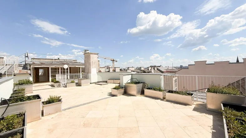 Helle Dachterrasse mit bepflanzten Metallkübeln und einem weiten Blick über die Dächer der Stadt.